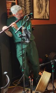 Man dressed in green playing flute at pub