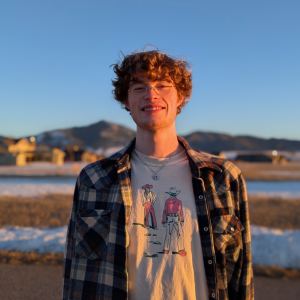 Henson Burk-Fawcett stands outdoors during sunset wearing a plaid flannel and smiling at the camera.