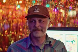 Devin Champlin with a neutral expression looking slightly off camera and wearing a red ball cap and a plaid button-up shirt.