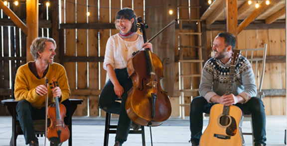 3 musicians, sitting in an otherwise empty barn, with their fiddle, cello, guitar